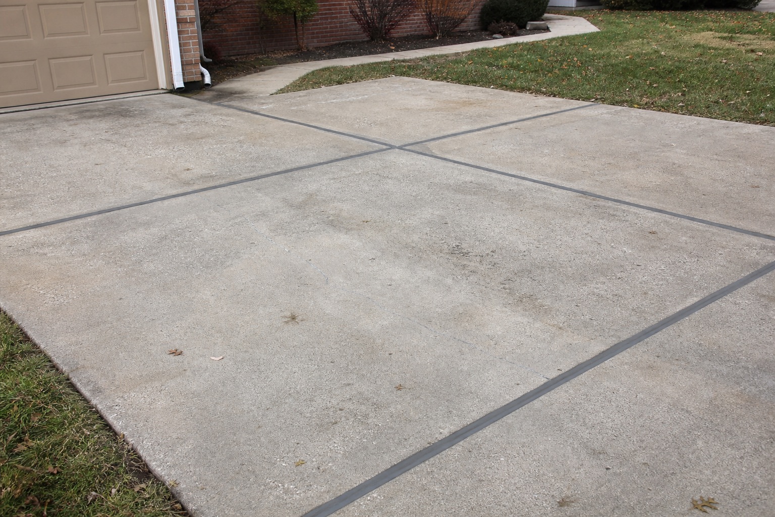 Older residential driveway with completed gray expansion-joint sealing