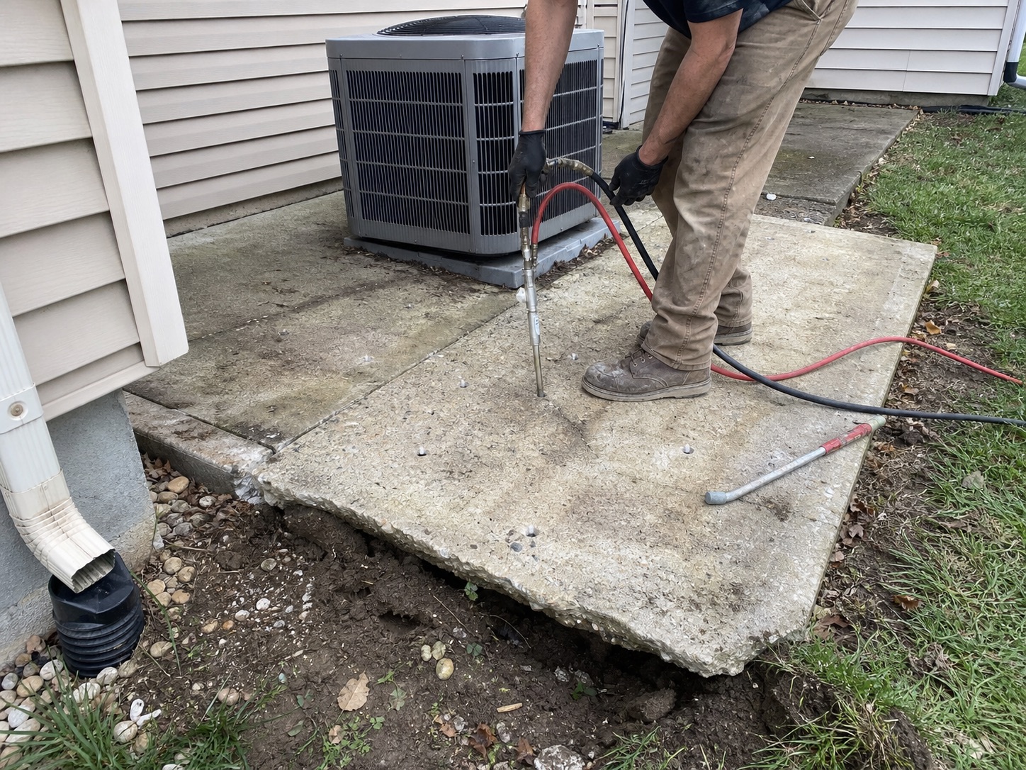 Technician placing polyurethane material beneath an unsupported outdoor utility slab